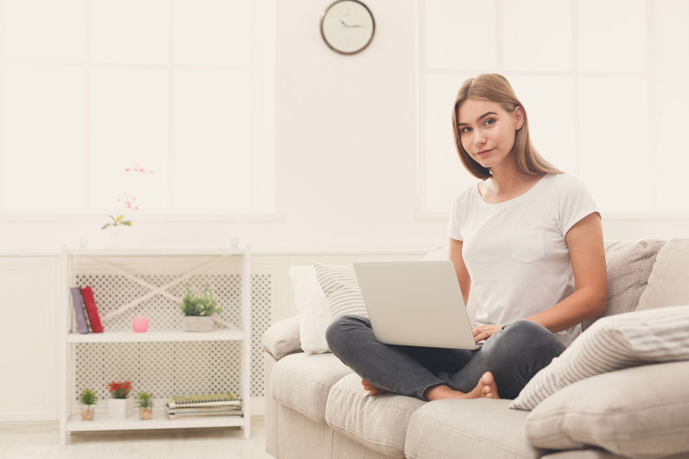 young-blonde-girl-chatting-laptop-sitting-beige-couch-looking-camera-freelancer-working-home-copy-space.jpg
